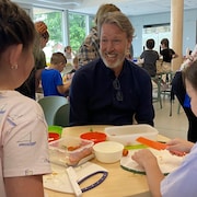 Ricardo est attablé avec des écoliers lors d'un atelier culinaire.